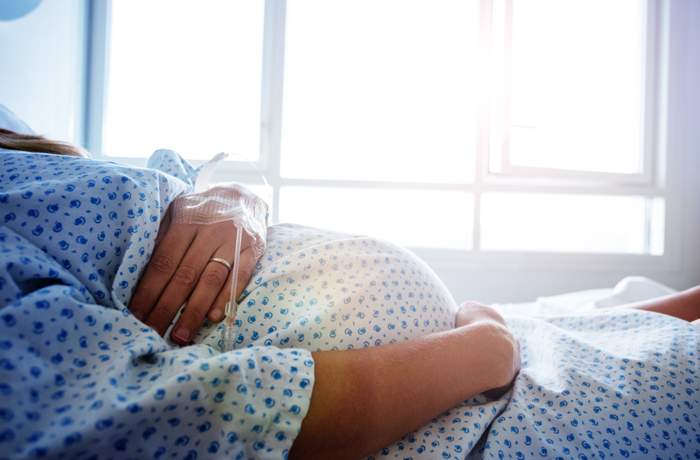 A pregnant woman in a surgical gown laying in a hospital bed